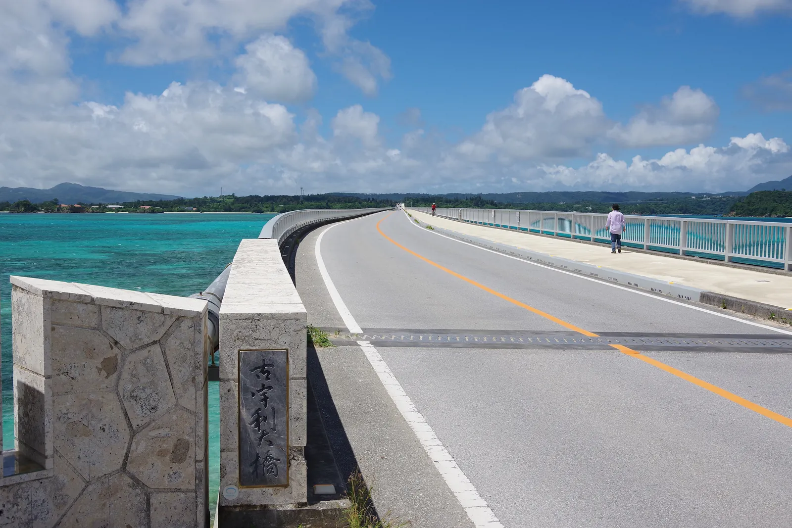 A road bridge over turquoise water on a sunny day with large white clouds; Kouri Bridge in northern Okinawa, not the park